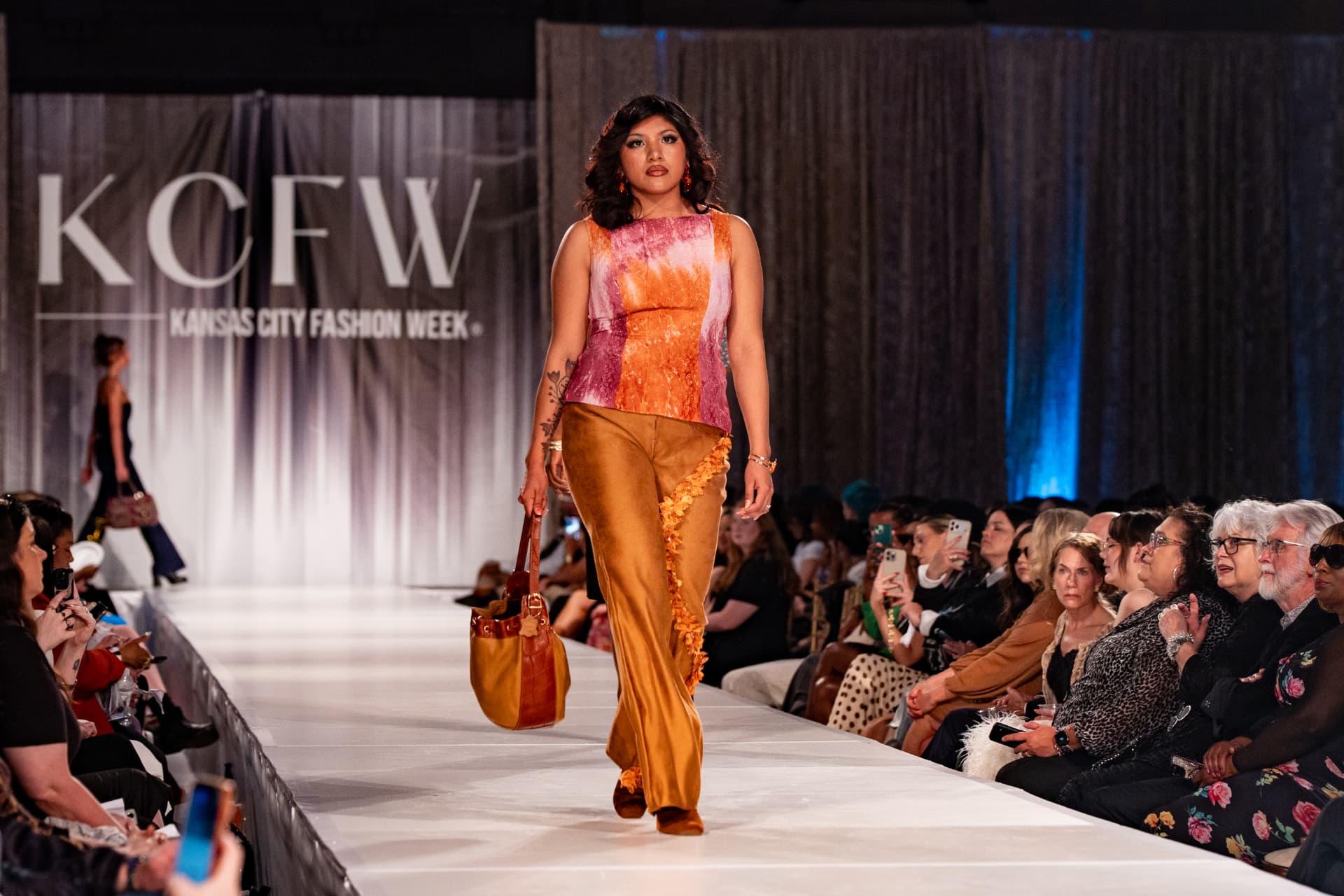 Model on the KCFW runway in a Range & Reverie sunset top and gold trousers